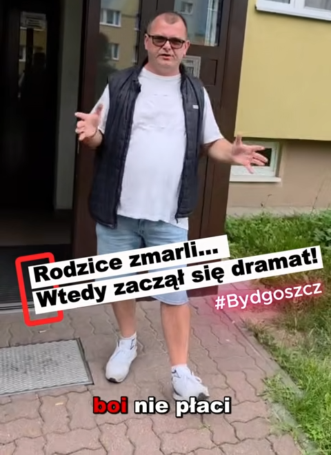 videoframe_4268 Mężczyzna z krótkimi włosami i w okularach przeciwsłonecznych stoi przed wejściem do budynku, gestykulując z podniesionymi rękami. Na zdjęciu widnieje napis w języku polskim: „Rodzice zmarli… Wtedy zaczął się dramat! #Bydgoszcz boi nie płaci..”.